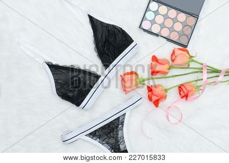 Black Set Of Lacy Underwear On White Fur. Orange Roses And Eye Shadow. Fashionable Concept
