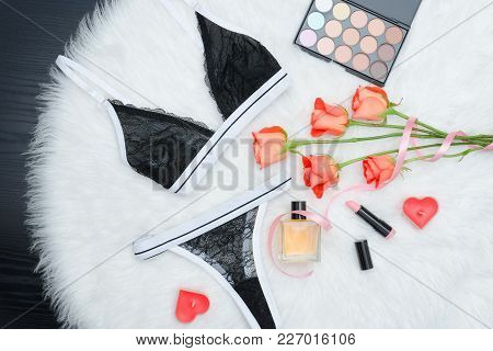 Black Set Of Lacy Underwear On White Fur. Orange Roses, Eye Shadows, Lipstick And Candles. Fashionab