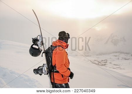 Front View Of Male Snowboarder Looking On The Beautiful Snowy Mountain Peaks Snd Cloudy Sky