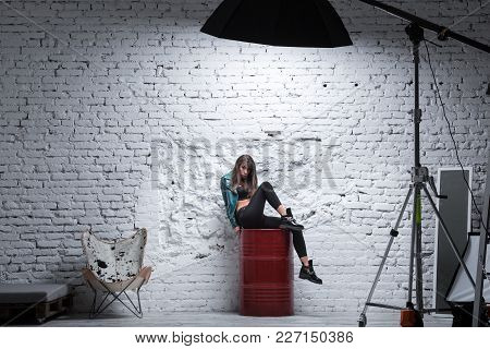 Stylish Brunette Woman Sitting On A Red Barrel Against White Grungy Brick Wall. Professional Photo S