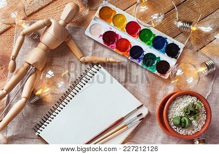 Top View Mockup With Notepad, Paints, Brushes, Flower, Wooden Dummy And Bulb On Wood And Fabric Back