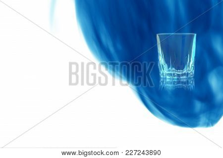 An Empty Shot Of Vodka Or Tequila On White Background Enveloped In Puff Of Blue Smoke. Place For You