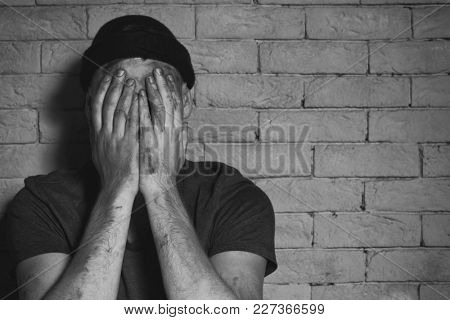 Hungry poor man crying near brick wall