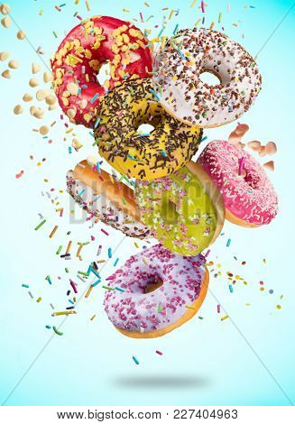 Tasty doughnuts in motion falling on pastel blue background, close-up.