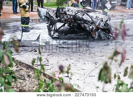 Burned Car After An Accident On The Road. Firefighters Standing Nearby. Reportage Picture Crowd In B
