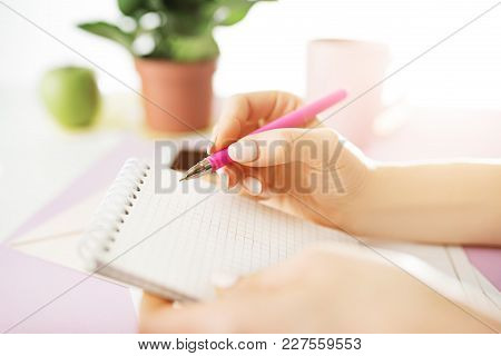The Female Hands Holding Pen. The Phone On Trendy Pink Desk.