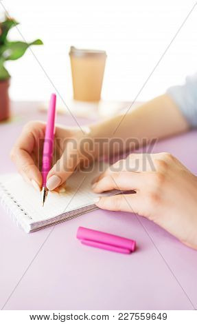 The Female Hands Holding Pen. The Phone On Trendy Pink Desk.