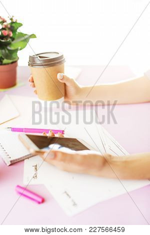 The Female Hands Holding Phone And Coffee On Trendy Pink Desk.