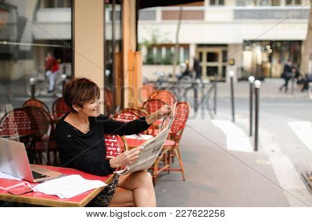 Woman Sitting At Table Of Street Cafe Skimmed Through New Newspaper. Female With Short Haircut Dress