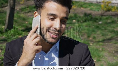Man Hold Phone In Hand And Talking With Mom. Son Has Dimple On Cheeks, Beard, Short Hair And Long No