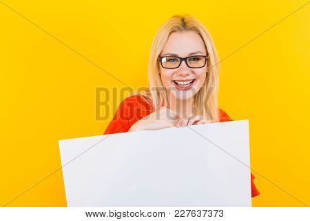 Portrait Of Attractive Happy Blonde Woman In Eyeglasses Isolated On Yellow Background Holding Emty B