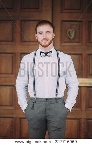 Stylish Groom In A White Shirt And Suspenders With A Red Beard