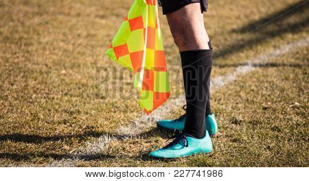 Football soccer arbiter assistant stands at sideline observing the match with flag at hands. Blurred green field background, close up.
