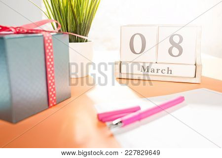 The Side View Of Orange Desk With Cup Of Coffee, Gift, Flowers And Notebook