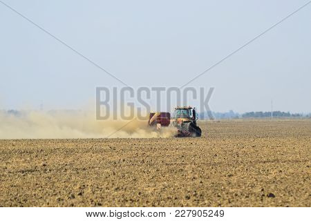 Tractor Rides On The Field And Makes The Fertilizer Into The Soil. Clouds Of Dust From The Dry Soil 