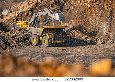 Hydraulic Excavator Loads Coal Into Body Of Large Yellow Mining Truck. Open Pit Mine Industry For An