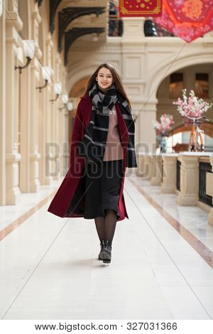 Full body portrait. Young beautiful woman in stylish in a long burgundy coat, indoor shop