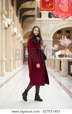 Full body portrait. Young beautiful woman in stylish in a long burgundy coat, indoor shop