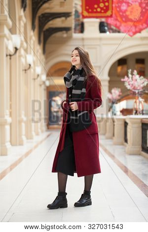 Full body portrait. Young beautiful woman in stylish in a long burgundy coat, indoor shop