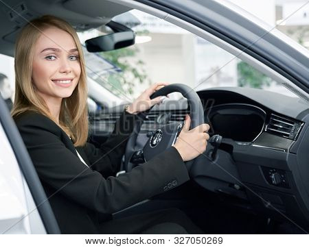 Young Woman Sitting In Right Handed Automobile, Looking At Camera And Smiling In Auto Showroom. Beau