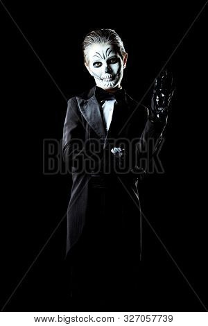 Portrait of a child boy with carnival make-up of a skeleton wearing elegant tail-coat. Studio shot over black background. Halloween. Dia de los muertos. The Day of the Dead.