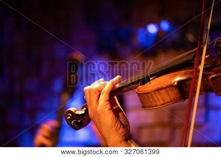 A Violinist Plays Classical Music On A Violin At A Concert With An Orchestra.