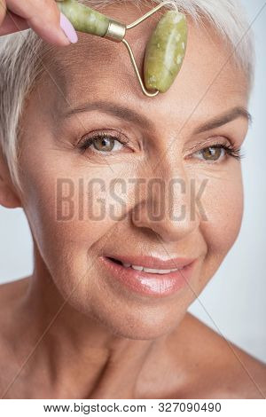 Close Up Of A Face Of Aged Woman Rolling Jade Roller On Her Fore Head