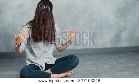 Funny Freak With Facial Hair And Glasses, Smart Monster Sitting On The Floor Against A Gray Wall.