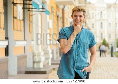 Attractive Boy In Blue Denim Clothes Looks In The Camera With Sincere Smile. Guy Stands In Philisoph