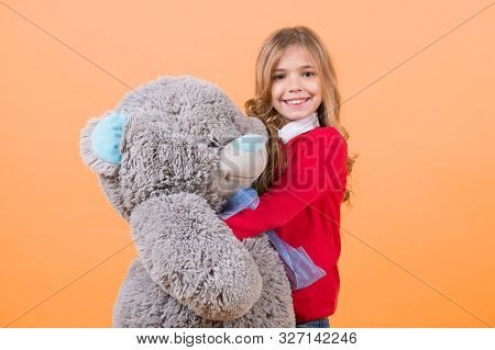 Child Smile With Grey Soft Toy. Girl Hug Big Teddy Bear On Orange Background. Holiday, Birthday, Ann