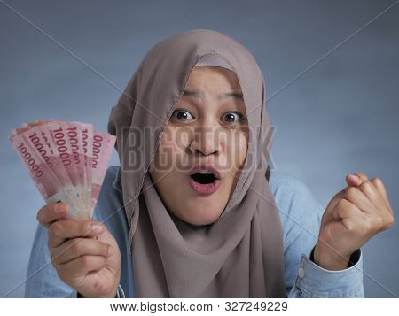 Portrait Of Indonesian Muslim Woman Holding Rupiah Money, Smiling Laughing Winning Gesture