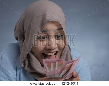 Portrait Of Indonesian Muslim Woman Holding Rupiah Money, Smiling Laughing Winning Gesture