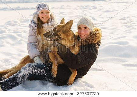 Joyful Teens Spend Time Together With Lovely Pet German Shepherd Dog On A Walk In The Winter Park On