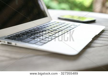 Laptop On A Wooden Table, With Cell Phone, Garden Or Outdoor Background. Flexi Work Concept.