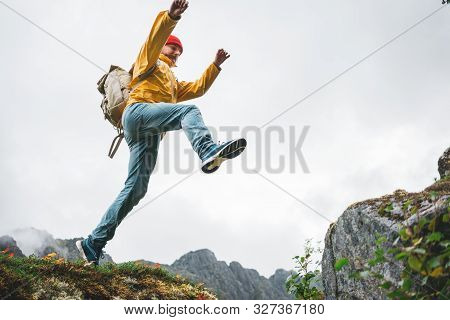 Adventure Tourist Jumping On Rocks Over Cliff. Brave Man Traveler Hiking Trail In Authentic Wilderne