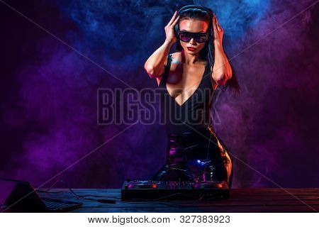 Young Sexy Woman Dj Playing Music. Headphones And Dj Mixer On Table. Colorful Smoke On Background