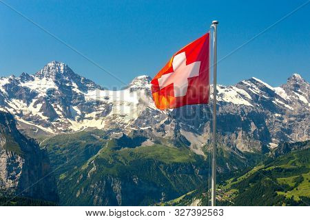 Swiss National Flag On A Background Of Snow-capped Mountains. Mannlichen.