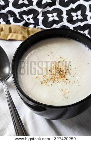 Cauliflower Soup (creme Du Barry) In Black Bowl On White Background With Black And White Cloth
