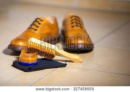 Pair Of Male Full Brogued Tan Oxford Shoes. Placed Together With Shoe Wax And Brush On Tiles Floor. 
