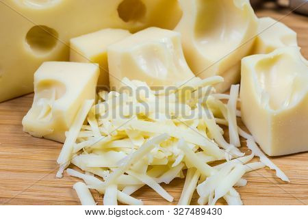 Grated Swiss-type Cheese Against Of Slices Of The Same Cheese On A Bamboo Wooden Cutting Board Close