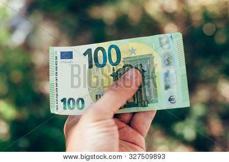 Male Hand Holding 100 Hundredth Euro Banknote On Green Background Outdoors, Closeup