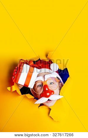Little Cheerful Santa In Glasses With A Red Nose And Mustache Gives A Gift, Getting Out Of The Ragge