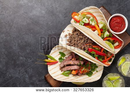 Set of mexican tacos with meat and vegetables in tortilla. And caipirinha cocktail. Top view on stone table. Flat lay with copy space