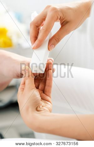 Woman podiatrist polishing nail of man during pedicure with file