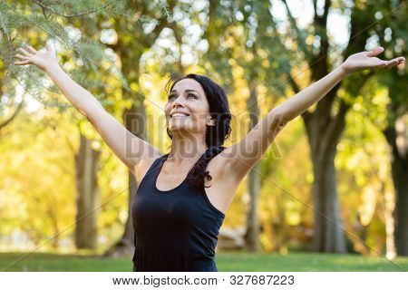 Happt brunette woman raising his arms in a park