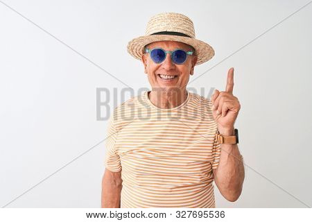 Senior man wearing striped t-shirt sunglasses and sumer hat over isolated white background surprised with an idea or question pointing finger with happy face, number one