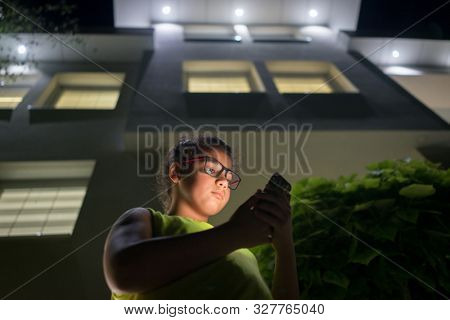 Boy with modile in front of house at night
