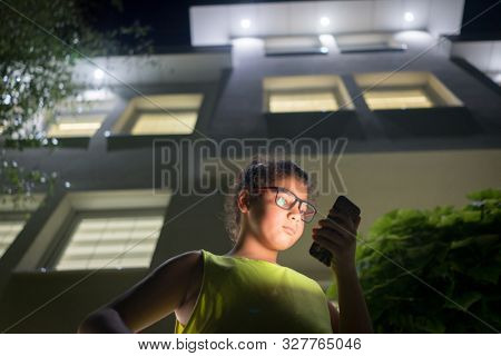Boy with modile in front of house at night