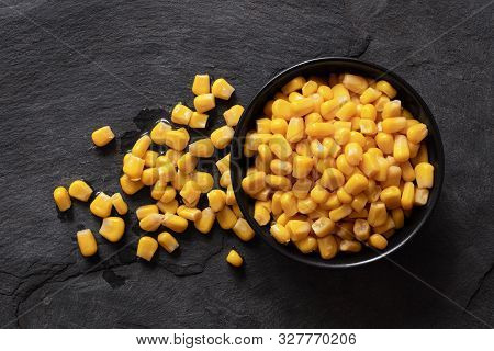 Canned Sweet Corn In A Black Ceramic Bowl Isolated On Black Slate Next To Spilled Sweet Corn. Top Vi