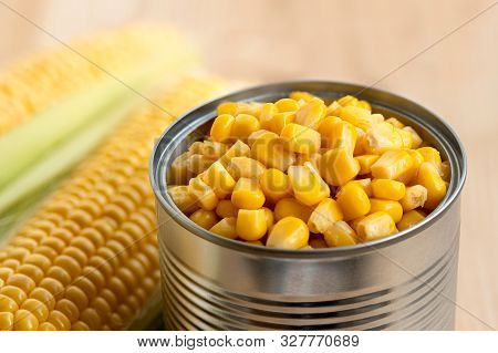 A Can Of Sweet Corn Next To Corn Cobs On Light Wood.